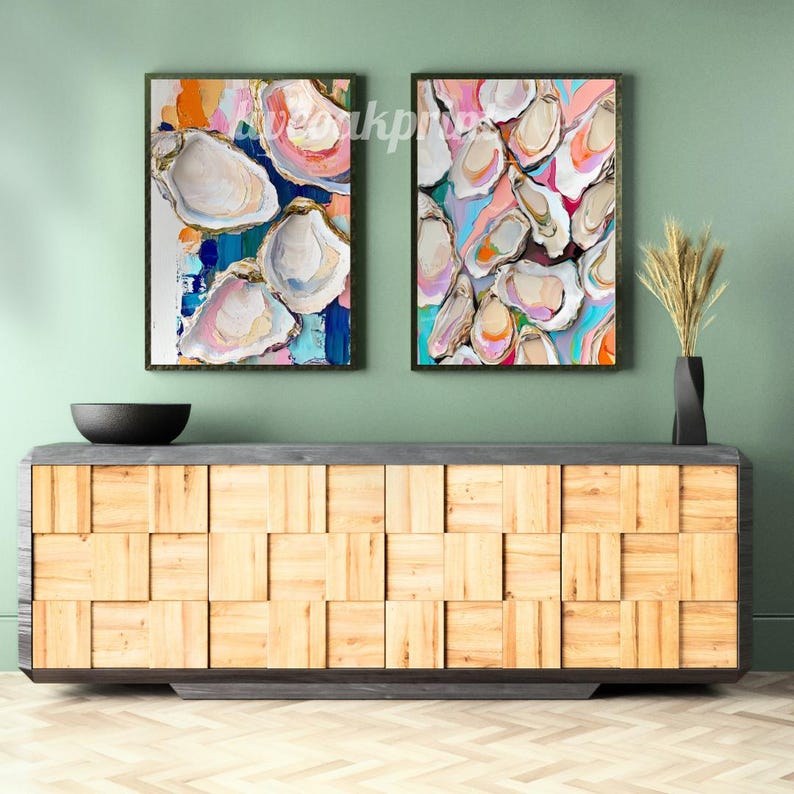 May include: Two abstract paintings of oyster shells in various shades of pink, blue, green, and yellow. The paintings are framed in black and hung on a green wall.