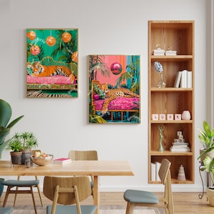 May include: Two framed prints of colourful jungle scenes with a cheetah and a tiger lounging on pink and green beds. The prints are hanging on a white wall above a wooden table with chairs.