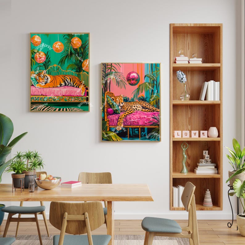 May include: Two framed prints of colourful jungle scenes with a cheetah and a tiger lounging on pink and green beds. The prints are hanging on a white wall above a wooden table with chairs.