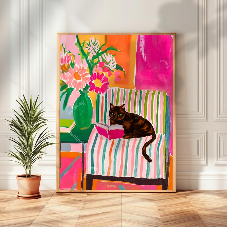 Op de afbeelding: Een ingelijste kunstdruk met een kat die een boek leest op een gestreepte stoel. Het kunstwerk heeft een levendig kleurenpalet met roze, oranje en groene tinten. Een vaas met bloemen staat naast de kat. De print zit in een houten lijst.