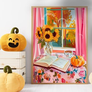 Op de afbeelding: Een schilderij van een raam met uitzicht op herfstbomen. Een vaas met zonnebloemen staat op een tafel met een boek en een kopje thee. Een kleine pompoen ligt op de tafel naast het boek.