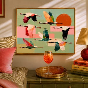 May include: A framed wall art print featuring a flock of stylized cranes in flight against a light green background with a large orange sun, pink rectangular accents, and various colorful patterns on the birds' wings and bodies.