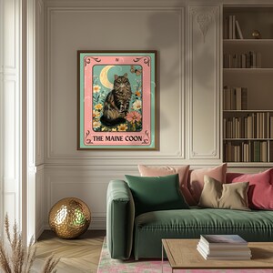 May include: A framed print featuring a Maine Coon cat in a tarot card design. The artwork showcases the cat amidst flowers, a crescent moon, and a butterfly, with the text "THE MAINE COON" at the bottom. The frame is brown, and the background is a mix of pink and teal.