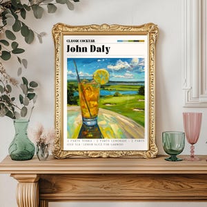 Może przedstawiać: Oprawiony wydruk przedstawiający koktajl John Daly. Obraz przedstawia szklankę koktajlu z plasterkiem cytryny na tle pola golfowego. Rama jest złota. Tekst brzmi "Classic Cocktail John Daly" ze składnikami.