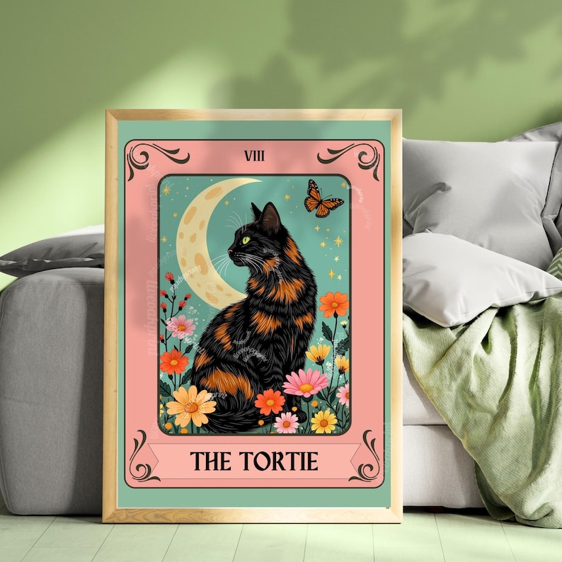 May include: A framed print featuring a black and orange tortoiseshell cat, labeled "THE TORTIE." The artwork includes a crescent moon, butterfly, and colorful flowers. The background is a teal color, and the frame is gold.