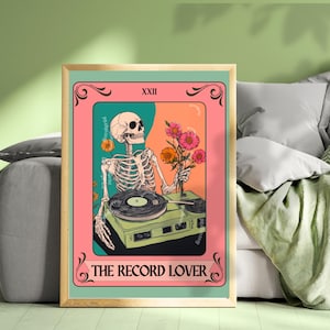 May include: A framed art print featuring a skeleton holding flowers and standing next to a record player. The artwork has a pink, orange, and teal color scheme with the text "THE RECORD LOVER" at the bottom.