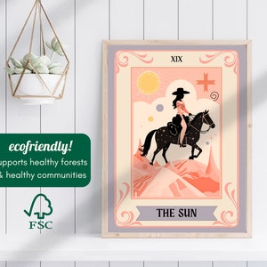May include: A vintage-style tarot card illustration featuring The Sun card, XIX, with a woman riding a horse in a desert landscape. The card is framed in a light grey frame.