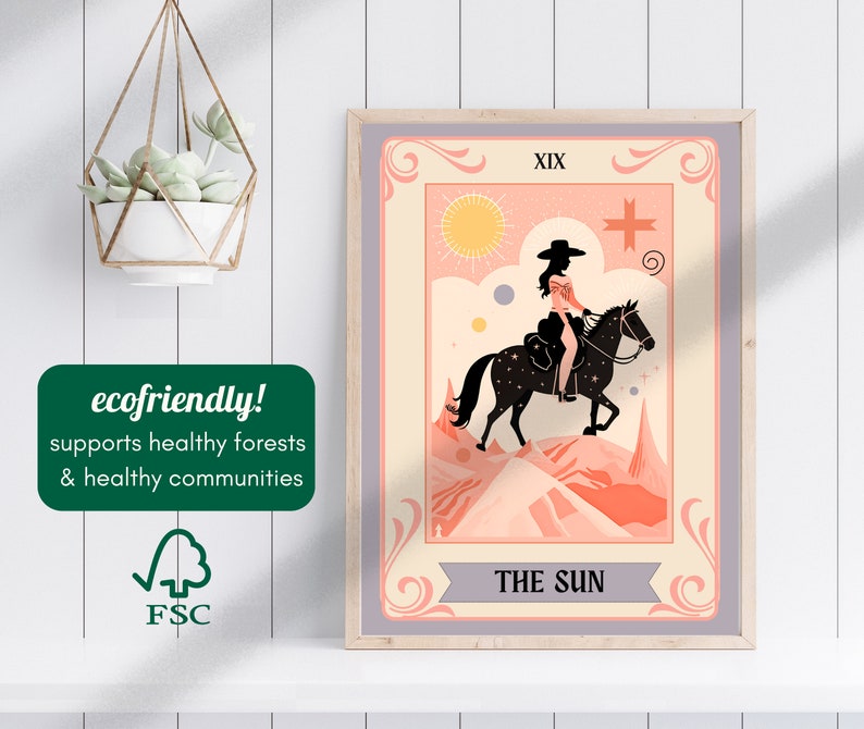 May include: A vintage-style tarot card illustration featuring The Sun card, XIX, with a woman riding a horse in a desert landscape. The card is framed in a light grey frame.