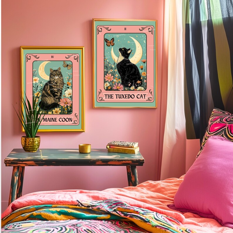 May include: Two framed art prints featuring cat illustrations. One print shows a Maine Coon cat, the other a Tuxedo cat, both set against a floral and crescent moon backdrop. The frames have gold borders, and the background is pink.