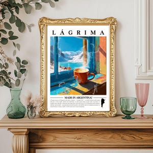 Könnte beinhalten: Gerahmter Kunstdruck mit einer Kaffeetasse auf einer Fensterbank mit Blick auf eine schneebedeckte Berglandschaft. Der Druck trägt die Aufschrift "LAGRIMA" und "MADE IN ARGENTINA!". Der Rahmen ist goldfarben.