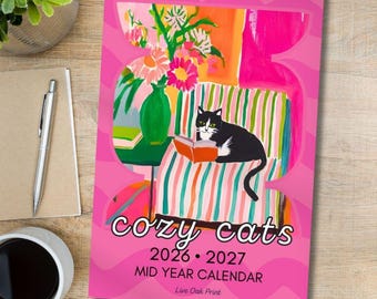 May include: A pink mid-year calendar with a black and white cat reading on a striped chair. The calendar reads "cozy cats 2026-2027" and features a colourful illustration of flowers in a vase.