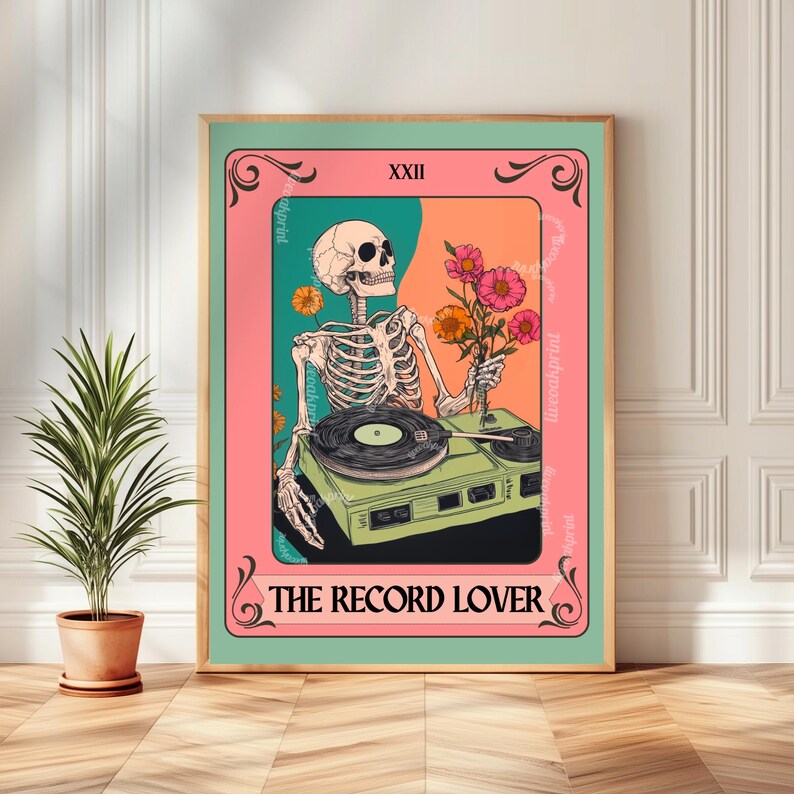 Op de afbeelding: Een ingelijste kunstprint met een skelet dat bloemen vasthoudt en een vintage platenspeler bedient. Het kunstwerk heeft een roze, teal en oranje kleurenschema, met de tekst "THE RECORD LOVER" onderaan en "XXII" bovenaan.