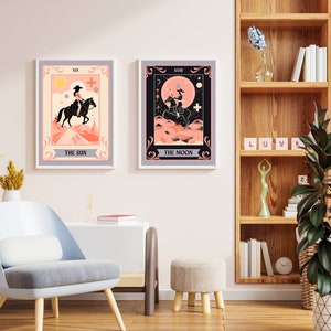 May include: Two tarot card prints with a pink and peach colour scheme. The prints are framed in a light grey frame and feature a woman riding a horse. The first print is titled "The Sun" and the second print is titled "The Moon".