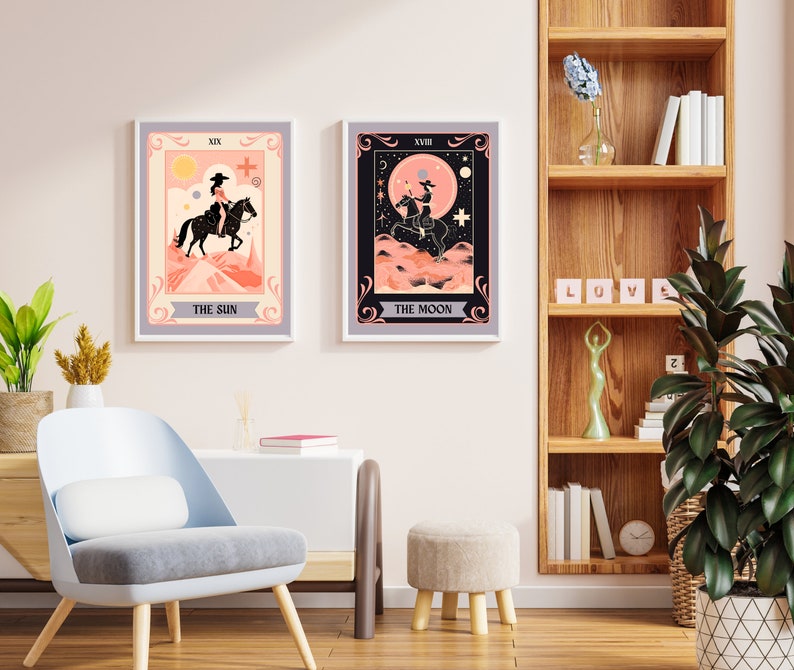 May include: Two tarot card prints with a pink and peach colour scheme. The prints are framed in a light grey frame and feature a woman riding a horse. The first print is titled "The Sun" and the second print is titled "The Moon".