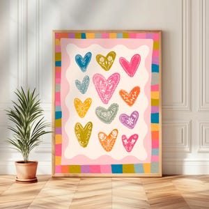 May include: A framed print with a pink background and a white border. The print features 15 colourful hearts with white floral designs. The hearts are arranged in a grid pattern. The frame has a wooden border with colourful stripes.