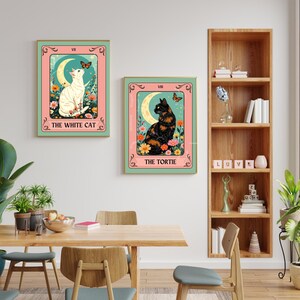 May include: Two framed art prints featuring cat illustrations in a tarot card style. One print shows a white cat, the other a tortoiseshell cat, both with floral and moon elements. The text on the prints reads "The White Cat" and "The Tortie".