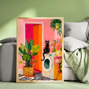 May include: A framed art print featuring a black cat with orange eyes perched on a washing machine. The artwork depicts a vibrant interior scene with a pink wall, an open orange doorway, and potted plants. A zebra-striped rug adds a playful touch.