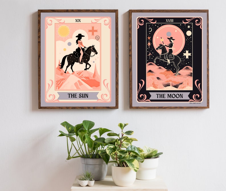 May include: Two framed tarot card prints, one depicting The Sun and the other The Moon. Both cards feature a woman riding a horse in a desert landscape. The Sun card has a yellow sun and a pink sky, while the Moon card has a black sky with a crescent moon and stars.