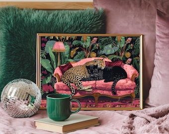 May include: A framed art print depicting a leopard and a black panther on a pink sofa, set against a tropical background. The print is in a gold frame. A green mug, a book, and a disco ball are in the foreground.