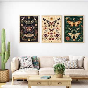 Op de afbeelding: Drie ingelijste prints met een donkere, een lichte en een groene achtergrond. Elke print toont een ander vlinderontwerp met bloemmotieven en hemelse elementen zoals manen en sterren.