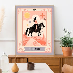 May include: A tarot card illustration depicting a woman riding a horse in a desert landscape. The card is titled "The Sun" and is numbered XIX. The illustration is in a vintage style with a pink and orange colour scheme.