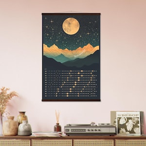 May include: A vertical wall calendar featuring a dark night sky with a large full moon and stars above layered mountain silhouettes in shades of orange, teal, and dark blue. The bottom section displays a lunar phase chart for each month.