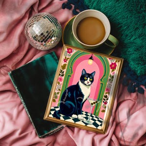 May include: A framed art print featuring a black and white cat with a martini glass. The artwork is set against a pink and green background with floral accents. A disco ball, a green teacup with coffee, and a velvet book are also in the image.