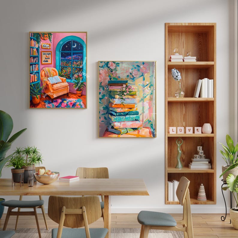 May include: Two colorful paintings depicting a cozy reading nook and a stack of books. The reading nook painting features a blue armchair, a bookshelf, and a window with a view of a city skyline. The book painting features a stack of colorful books with flowers and leaves surrounding them. The paintings are displayed on a white wall in a dining room setting with a wooden table and chairs.