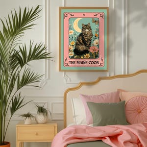 May include: A framed print featuring a Maine Coon cat in a tarot card design. The artwork has a teal background with a pink border, a crescent moon, and flowers. The text "THE MAINE COON" is at the bottom.