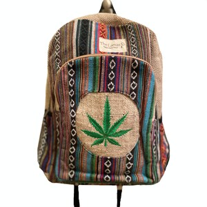 May include: A multi-colored striped hemp backpack with a large embroidered green marijuana leaf on the front. The backpack has a brown leather zipper pull and a brown leather tag that says "The Lamas Handmade in Nepal".