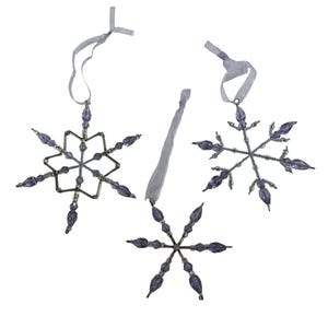May include: Three snowflake ornaments crafted from silver-toned wire and translucent purple beads. Each ornament features a unique geometric design and includes a light purple ribbon loop at the top for hanging, creating a decorative set.