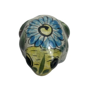 May include: Hand-painted ceramic frog figurine with a blue and yellow flower design. The frog is sitting on a white background.