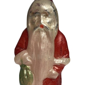 May include: A vintage glass Christmas ornament depicting Santa Claus in a red and white suit, holding a green bag. The ornament has a silver metallic finish and a silver wire hanger.