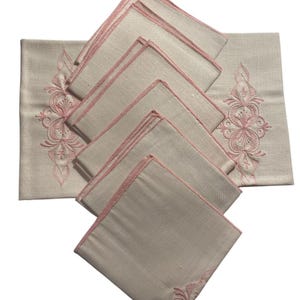May include: Set of 10 linen napkins with pink embroidered floral designs. The napkins are folded and arranged in a stack.