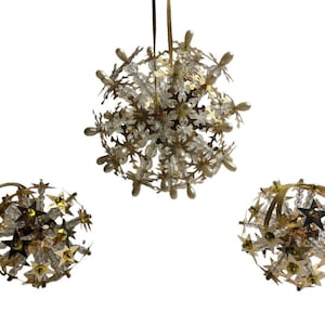 May include: Three gold Christmas ornaments with a starburst design. The ornaments are made of metal and have clear beads and gold stars.