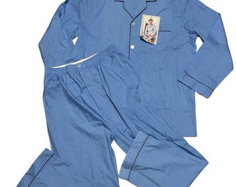 Puede incluir: Un conjunto de pijama azul claro que consta de una camisa de manga larga con botones y cuello de solapa, junto con un pantalón largo a juego. Ambas piezas presentan un ribete azul marino oscuro en los bordes. Una etiqueta está unida a la camisa.