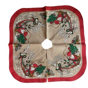 May include: A beige Christmas tree skirt with a red border. The skirt features a repeating pattern of Santa Claus riding in a sleigh pulled by reindeer. The reindeer are white with brown antlers.