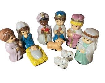 Könnte beinhalten: Eine Krippe aus Keramik mit Figuren des Jesuskindes, Maria, Josef, den drei Weisen und Schafen. Die Figuren sind in Pastellfarben mit goldenen Akzenten bemalt. Das Jesuskind liegt in einer gelben Krippe.