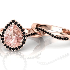 May include: A pear-shaped engagement ring set with a pink gemstone surrounded by a halo of black diamonds. The matching wedding band is a twisted band with black diamonds.