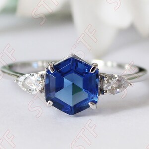 May include: A silver ring with a blue hexagonal gemstone and two smaller clear pear-shaped gemstones on either side.