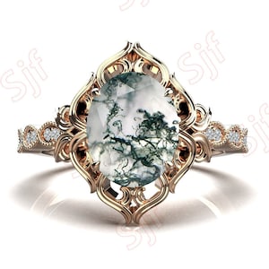 May include: A gold ring with a large oval-shaped moss agate gemstone set in a filigree design. The ring band is accented with small diamonds.