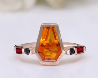 May include: A gold ring featuring a large orange gemstone in a geometric setting. The ring is accented with smaller red and black gemstones.