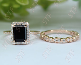 May include: A black diamond engagement ring set with a square emerald cut stone surrounded by a halo of smaller diamonds. The matching wedding band features a delicate row of round diamonds.