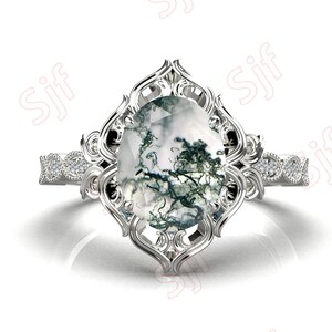 May include: A silver ring with a large, oval-shaped moss agate gemstone set in a filigree design. The ring has a band of smaller diamonds.