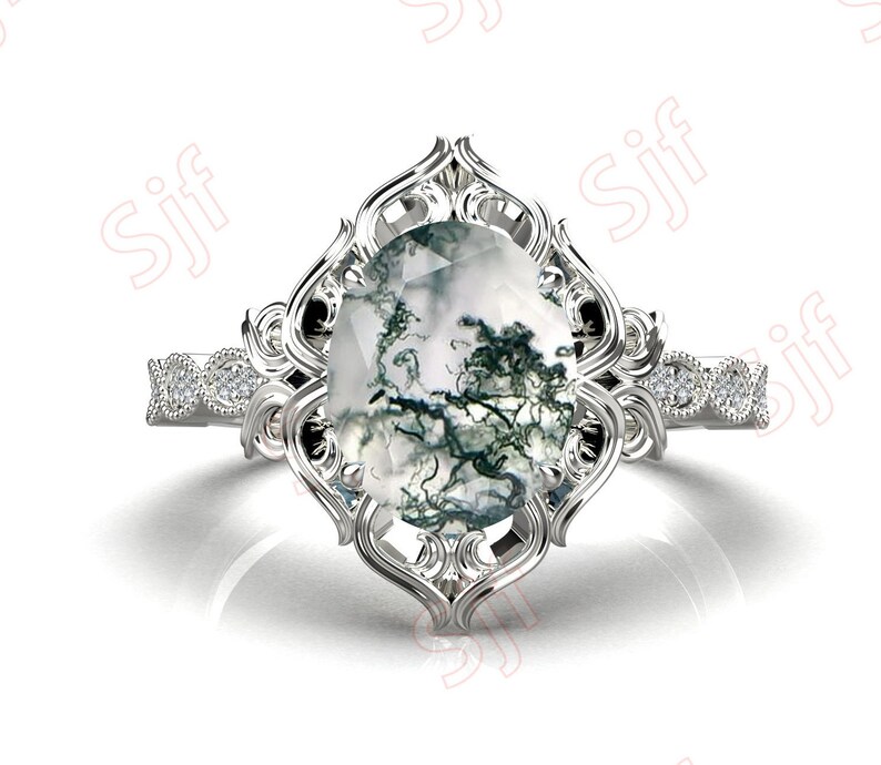 May include: A silver ring with a large, oval-shaped moss agate gemstone set in a filigree design. The ring has a band of smaller diamonds.