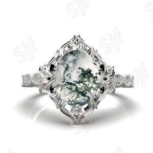 May include: A silver ring with a large, oval-shaped moss agate gemstone set in a delicate, ornate filigree design. The band is accented with small, sparkling diamonds.