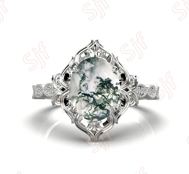 May include: A silver ring with a large, oval-shaped moss agate gemstone set in a delicate, ornate filigree design. The band is accented with small, sparkling diamonds.
