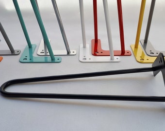 May include: A set of 10 hairpin table legs in various colors, including orange, teal, silver, white, red, yellow, gray, and black. The legs are made of metal and have a hairpin shape. The legs are arranged in a row, with the black leg in the foreground.