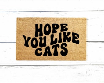 May include: A brown coir doormat with the text "HOPE YOU LIKE CATS" in black, stylized lettering.