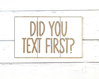 May include: A rectangular sign with a white background and a thin brown border. The text DID YOU TEXT FIRST? is printed in large, brown, sans-serif capital letters across the center of the sign, divided by two vertical lines.